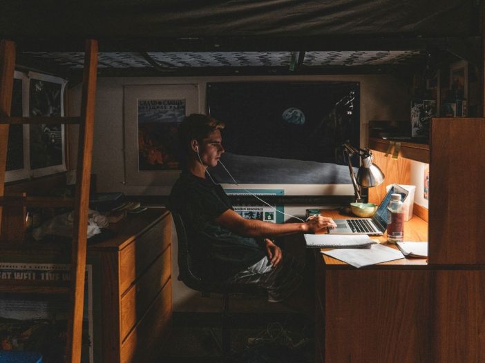 Man at his computer under a loft bed, mapping out a three-year plan.