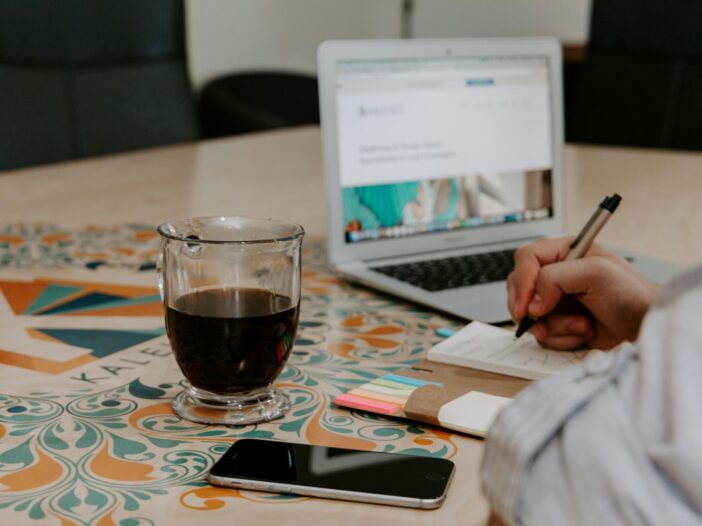 A cup of coffee, a notebook, and a person writing on a notepad, struggling to push through writer's block.