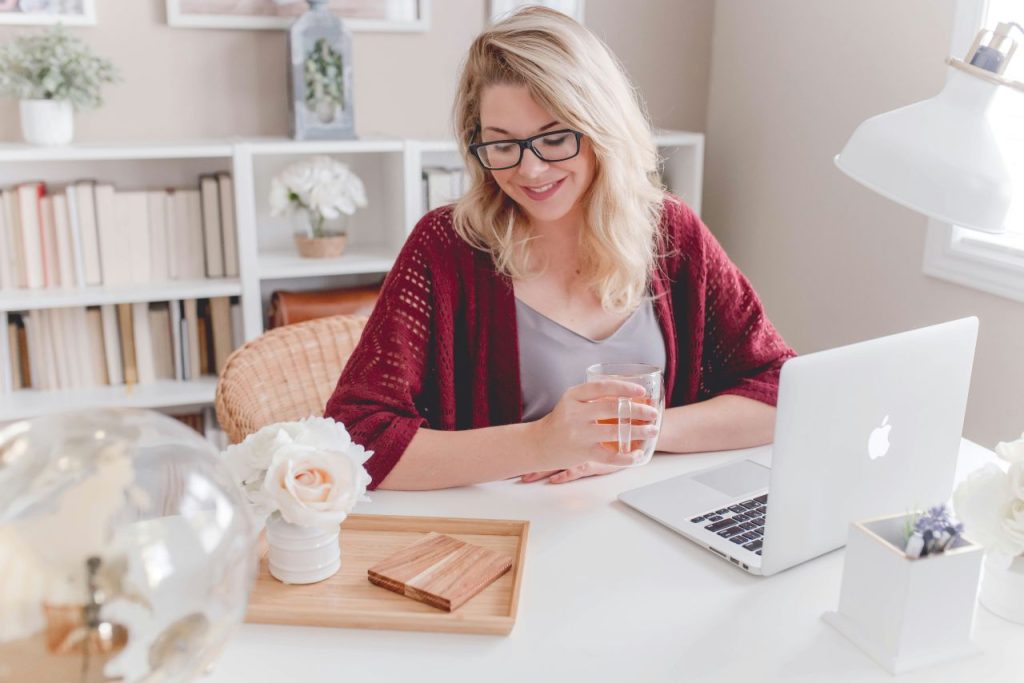 Woman smiles over a hot drink and laptop, proud of drafting a novel in a month.