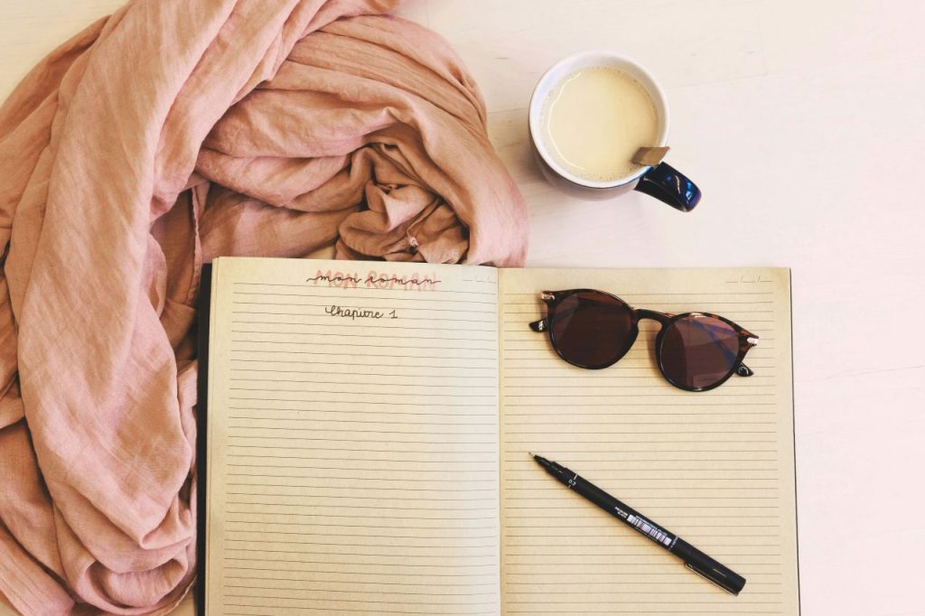 Open notebook with pen and sunglasses, ready for summer writing sprints.