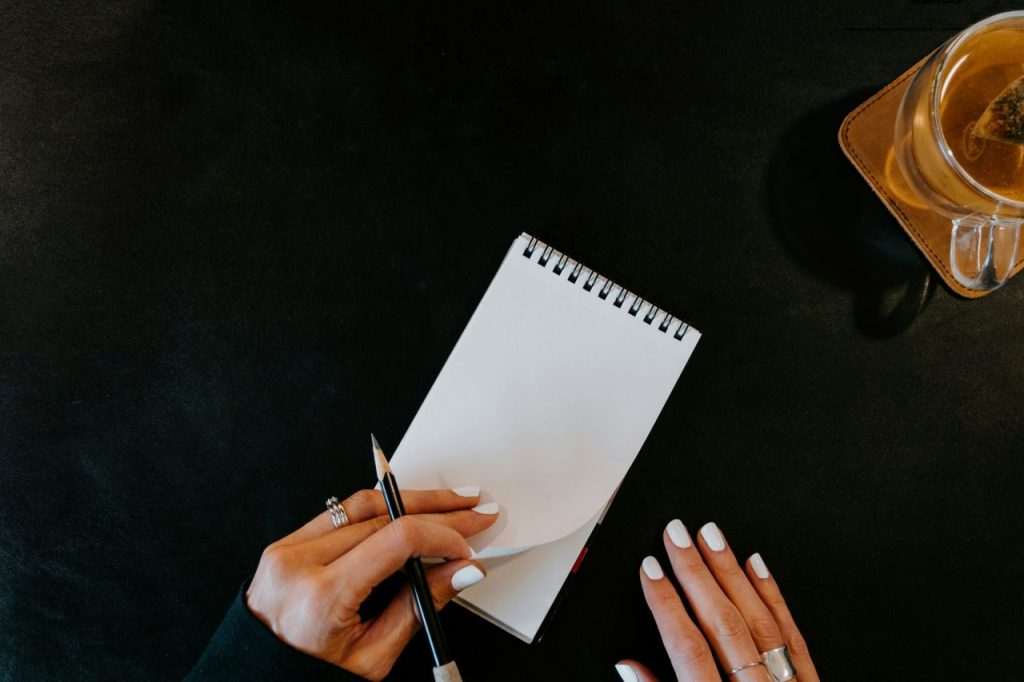 Hands poised over a spiral notebook, focusing on how to write better one line at a time.