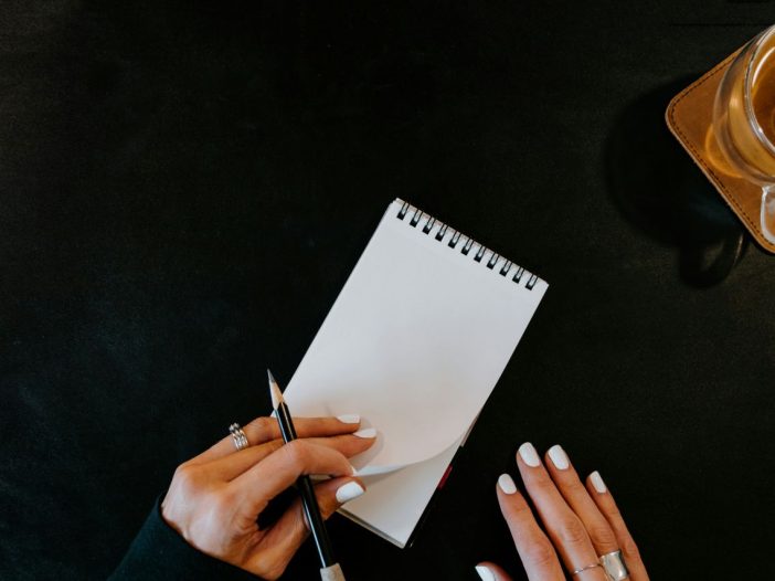 Hands poised over a spiral notebook, focusing on how to write better one line at a time.