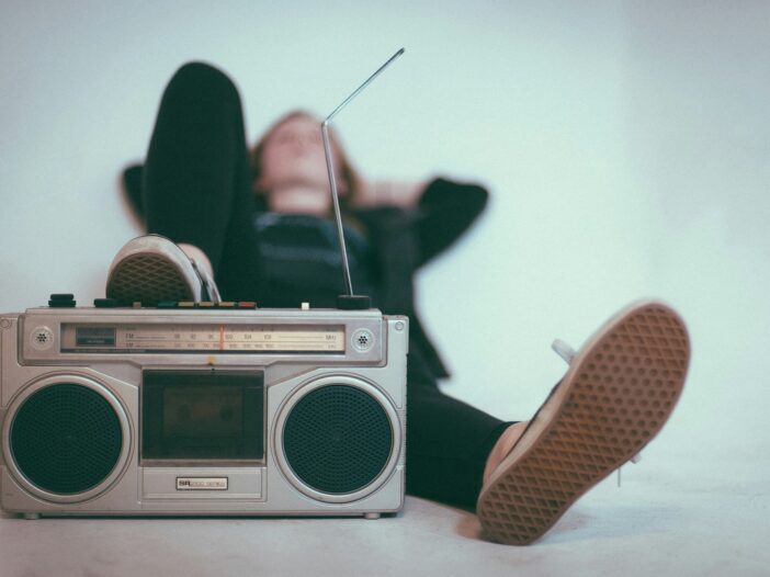 A person lying on their back with an old-school cassette player in the foreground, evoking nostalgia and the storytelling essence of music journalism.