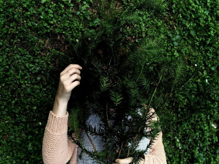 Visual metaphor for imposter syndrome—a person concealing themselves behind a leafy plant.